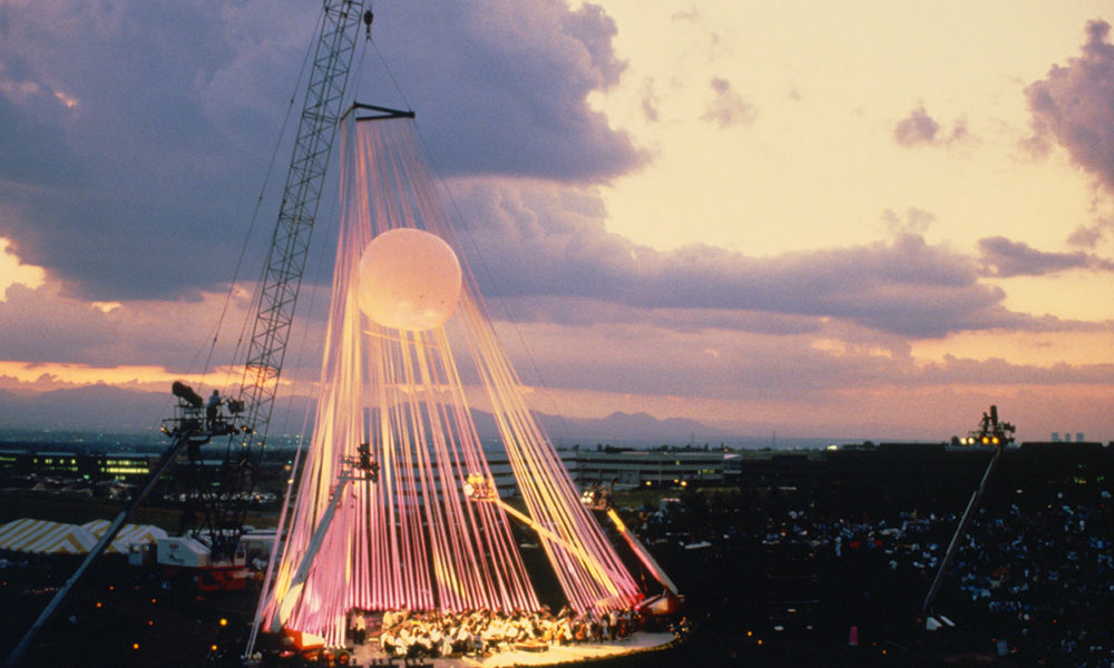 A crane is used to hang an illuminated cover over the temporary stage at fiddler's green prior to it becoming a formalized venue. The symphony is playing
