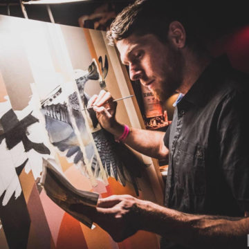 artist AJ Davis paints on a wooden panel in his studio in dim, but focused light.