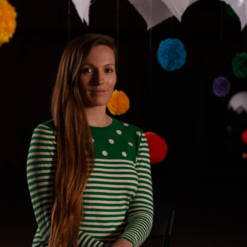 artist, tiffany matheson, sits in one of her art installations featuring colorful pom poms floating in space